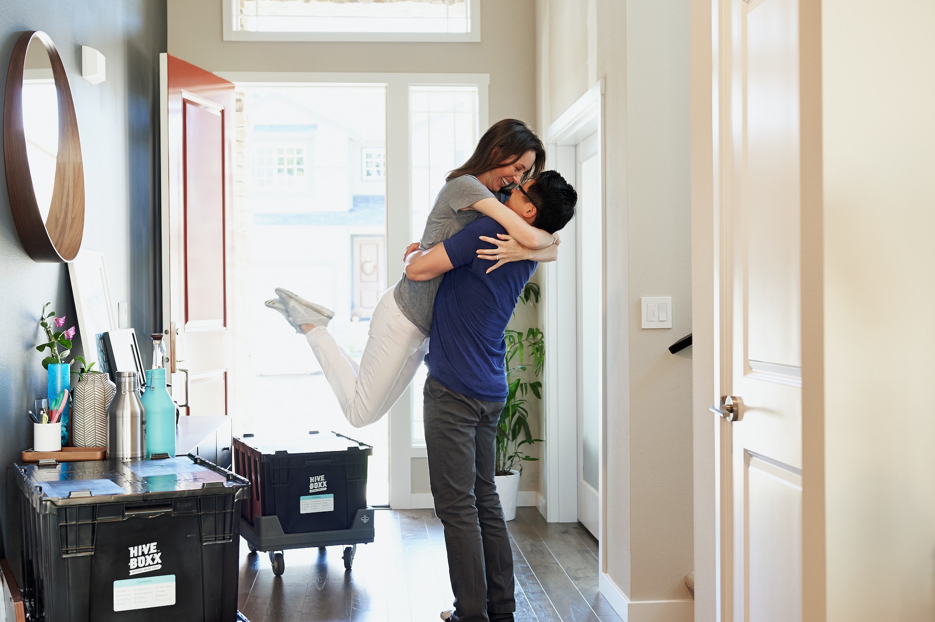 Couple embracing in hallway in front of open front door surrounded by moving boxes.